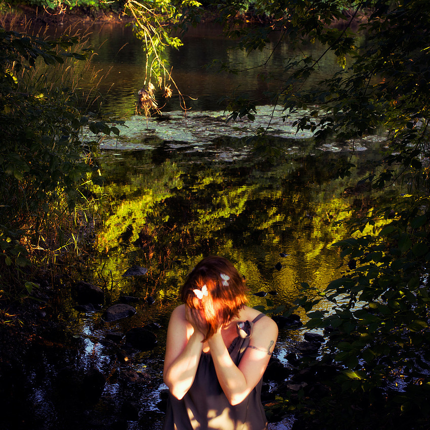 Photograph of woman covering hands with water and reflection behind her.