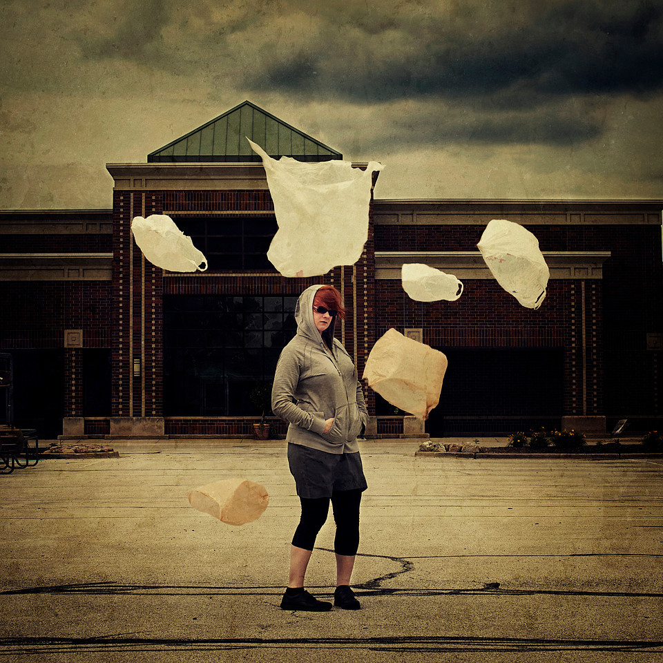 Woman standing in an abandoned parking lot with plastic bags floating around her.
