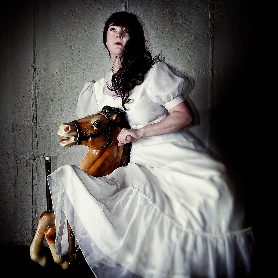 Conceptual portrait of woman on horse toy.