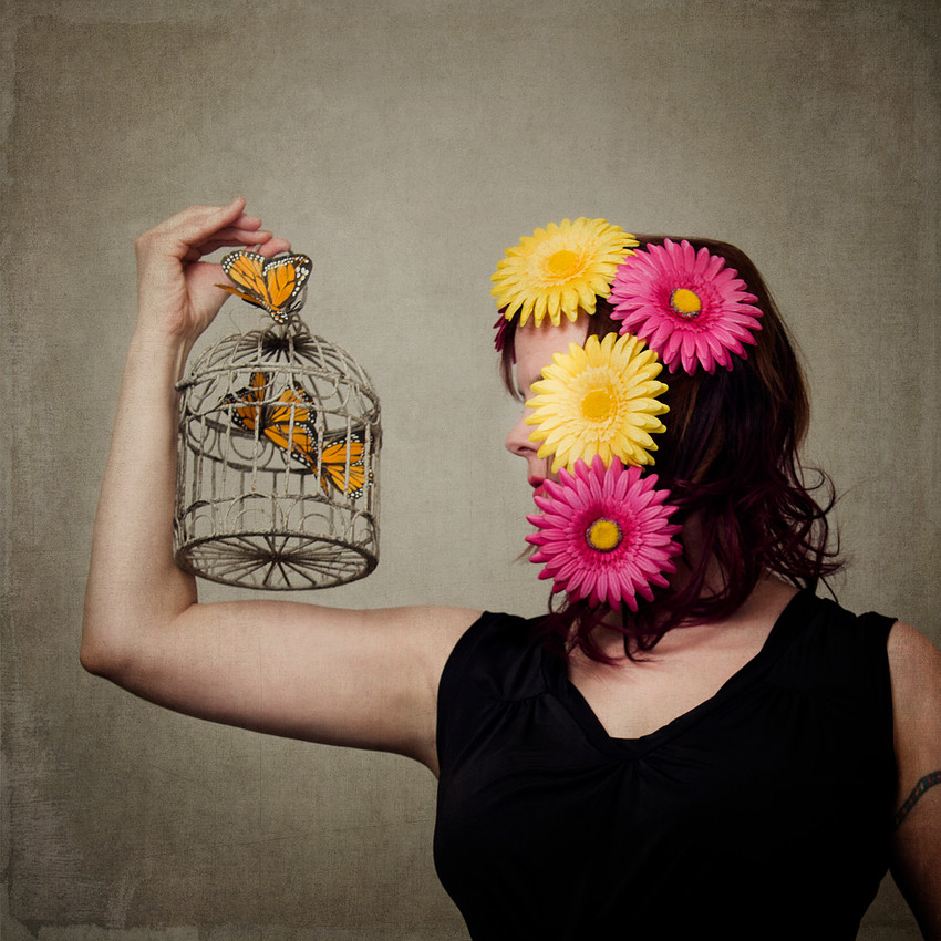 Fine art portrait, fashion photograph woman with flowers in hair and a birdcage with monarch butterflies.