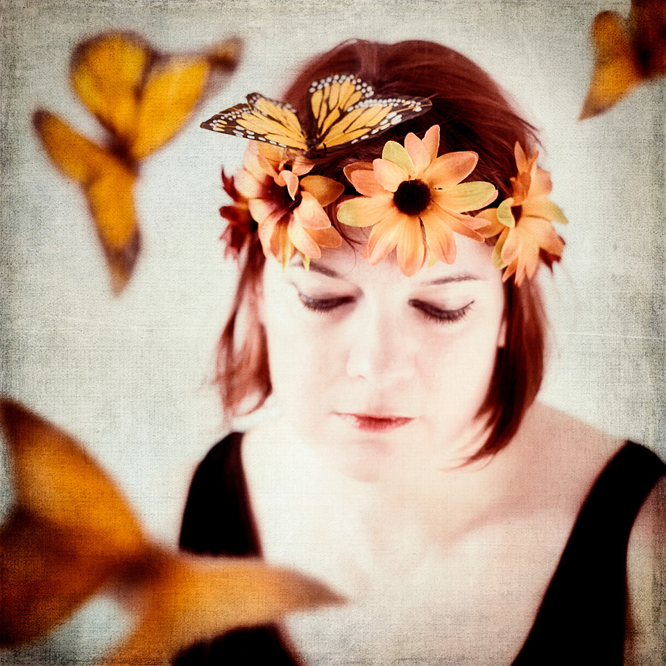 Portrait photograph of woman with monarch butterflies and orange flowers.