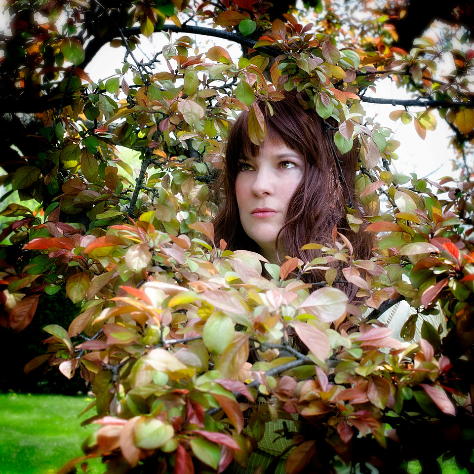 portrait photograph of woman with long brown hair surrounded by leaves.